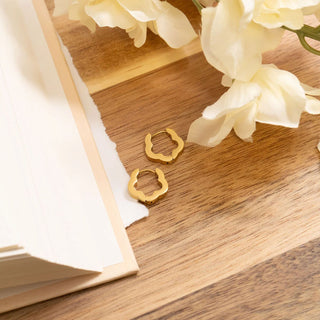 Gold earrings on a wooden surface with white flowers