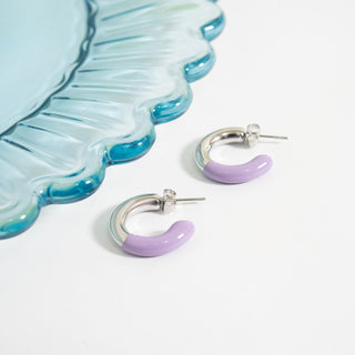 Purple hoop earrings on a white surface with a blue decorative plate.