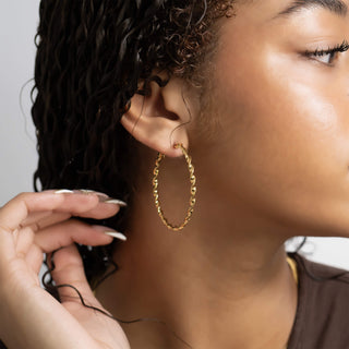 Close-up of a person wearing a gold hoop earring with a neutral background