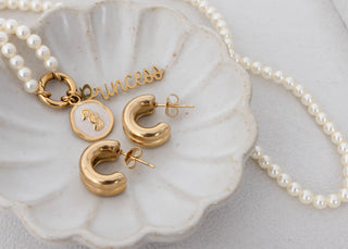 Gold 'princess' necklace and earrings on a shell with pearls.