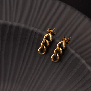 Gold chain earrings on a black textured surface