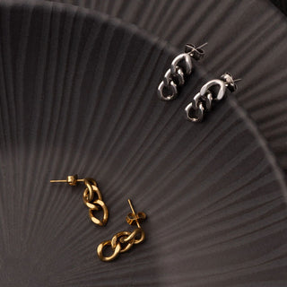 Pair of gold and silver chain-style earrings on a textured dark surface