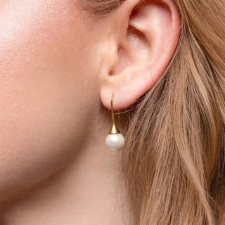 Close-up of an ear wearing a pearl earring with a gold hook.