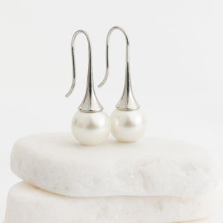 Pearl earrings on a white marble surface with a light gray background