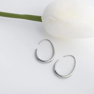 Silver hoop earrings on a light surface with a white flower and green stem.