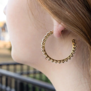 Gold hoop earring worn by a person with a blurred outdoor background