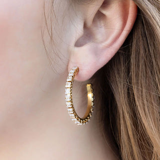 Gold hoop earring with embedded stones worn by a person