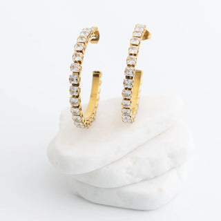 Gold hoop earrings with clear stones on a white marble surface