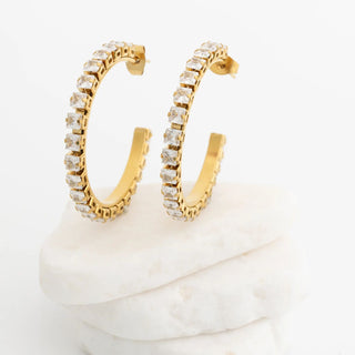 Gold hoop earrings with clear gemstones on a white surface