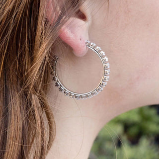 Close-up of a person wearing a silver hoop earring with small stones.