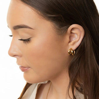 Close-up of a woman wearing gold hoop earrings with a neutral background