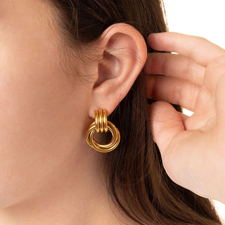 Gold hoop earrings worn by a person with a hand adjusting the earring.