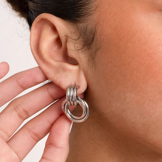 Close-up of a silver earring worn on an ear with a neutral background