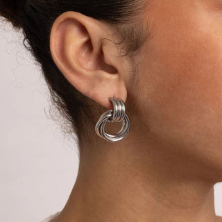 Close-up of an ear wearing a silver earring with a plain background