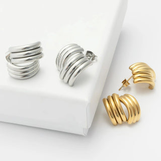 Pair of silver hoop earrings and gold cuff on a white background