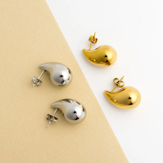 Gold and silver bird-shaped earrings on a beige and white background