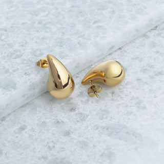 Gold teardrop-shaped earrings on a light marble background
