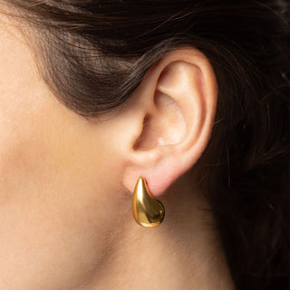 Gold teardrop earring worn on an ear with a neutral background