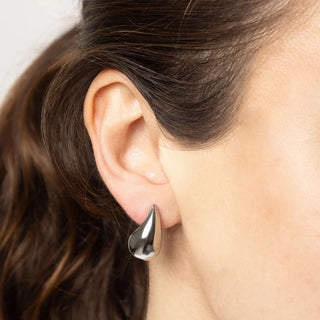 Close-up of an ear wearing a silver teardrop earring with blurred background