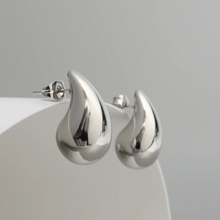 Silver earrings on a white stand with a gray background