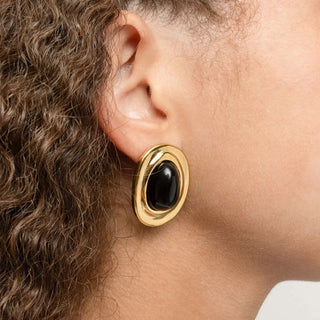 Gold Black Enamel Stud Earrings with a black gemstone worn by a person with curly hair.