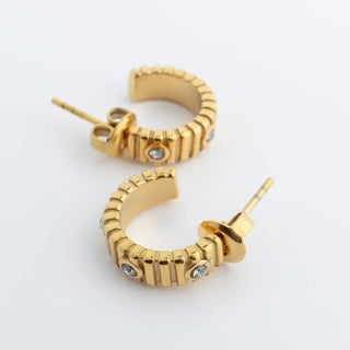 Gold hoop earrings with embedded stones on a light gray background