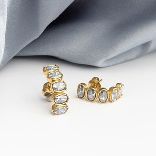 Gold Oval Stone Huggie Earrings with clear stones on a light gray fabric background