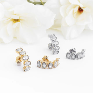 Gold and silver stud Oval Stone Huggie Earrings on a white background with flowers.