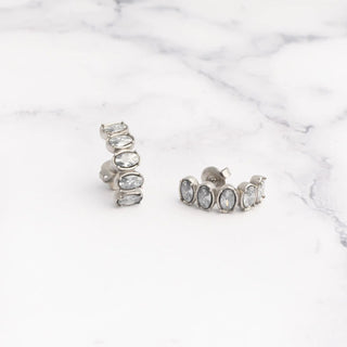 Pair of silver Oval Stone Huggie Earrings with clear stones on a marble surface