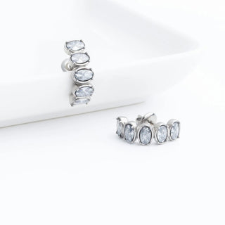 Pair of silver Oval Stone Huggie Earrings with clear gemstones on a white background