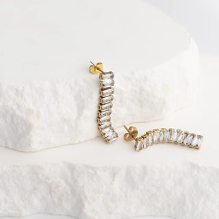 Gold and crystal earrings on a white textured surface