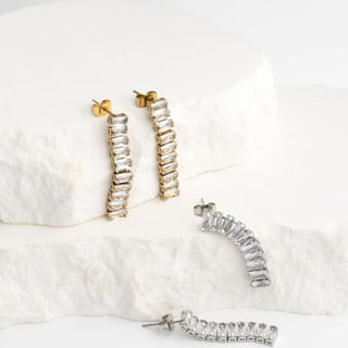 Pair of silver hoop earrings with clear gemstones on a white textured surface