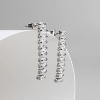 Silver hoop earrings with clear gemstones on a white stand against a gray background