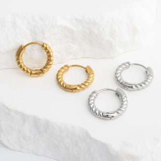 Four hoop earrings in gold and silver on a white fabric background