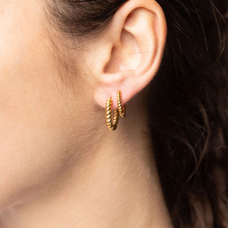 Close-up of a person wearing gold hoop earrings with a blurred background