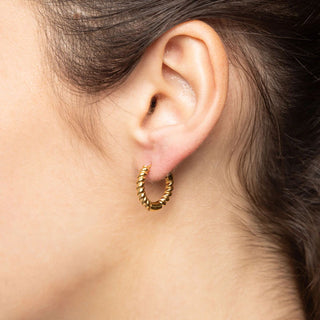 Close-up of an ear wearing a gold hoop earring with a neutral background