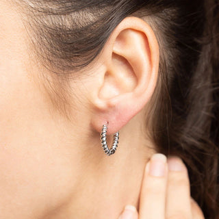 Close-up of an ear wearing a silver hoop earring with a blurred background