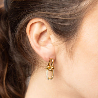Gold hoop earring with small diamonds worn by a person.
