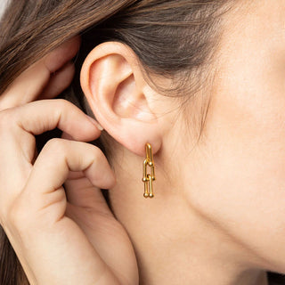 Gold chain earring worn by a person with hand near ear