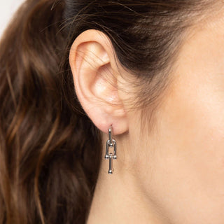 Close-up of an ear wearing a silver earring with a cross pendant.