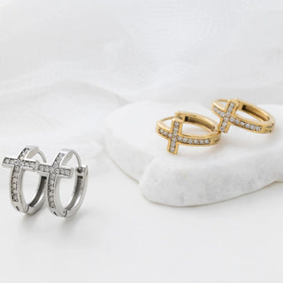 Pair of silver hoop earrings and gold cross-shaped rings on a white surface