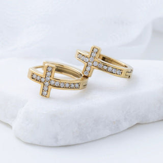 Two gold cross huggies with cz accents on a white surface