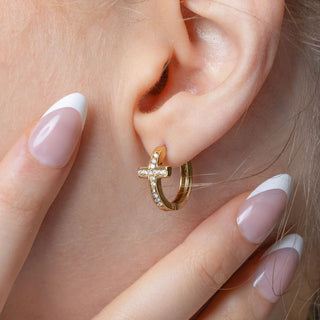 Gold cross hoop earring with cz stones worn by a person.