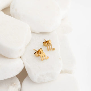 Gold letter earrings on a white stone background