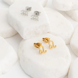 Gold Zodiac Leo earrings on a white stone surface