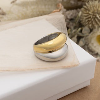 Two-tone gold and silver ring on a white cushion with a natural background