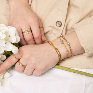 Close-up of hands wearing gold jewelry with a beige jacket and white flowers in the background