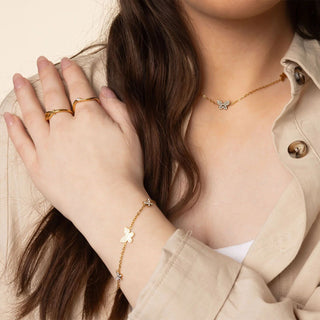 Person wearing gold jewelry including a necklace, bracelet, and ring on a neutral background