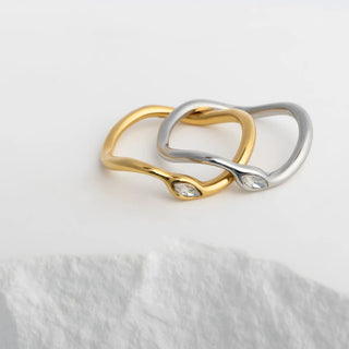 Two interlocking rings, one gold and one silver, on a white fabric background.