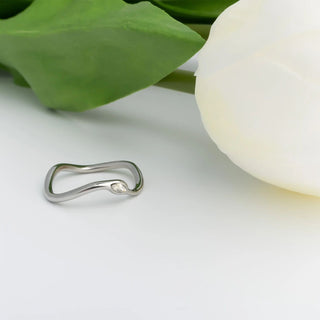 Silver earring on a white surface with a white flower and green leaves in the background
